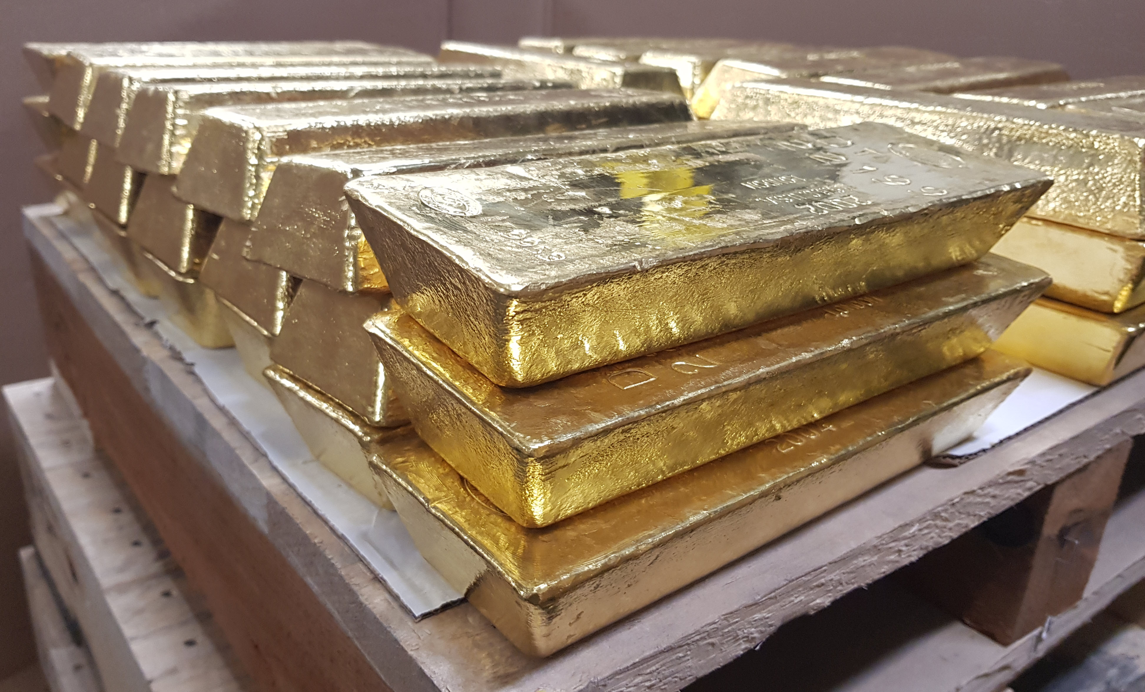 Gold wholesale bars stacked on a pallet within a vault